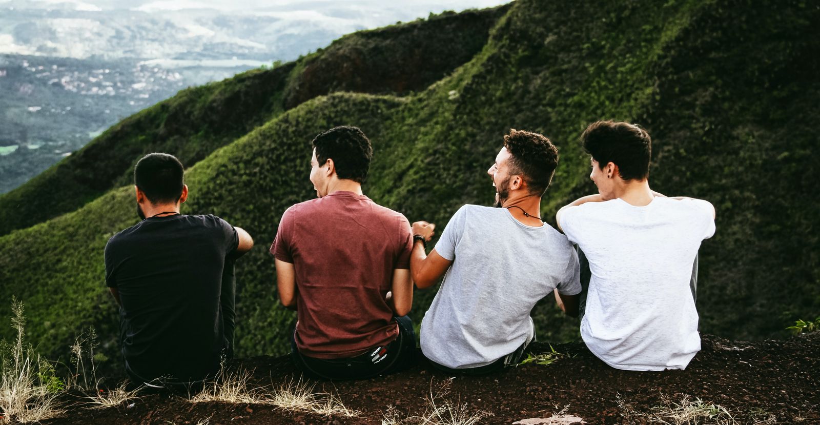 four guys sitting on mountain laughing together