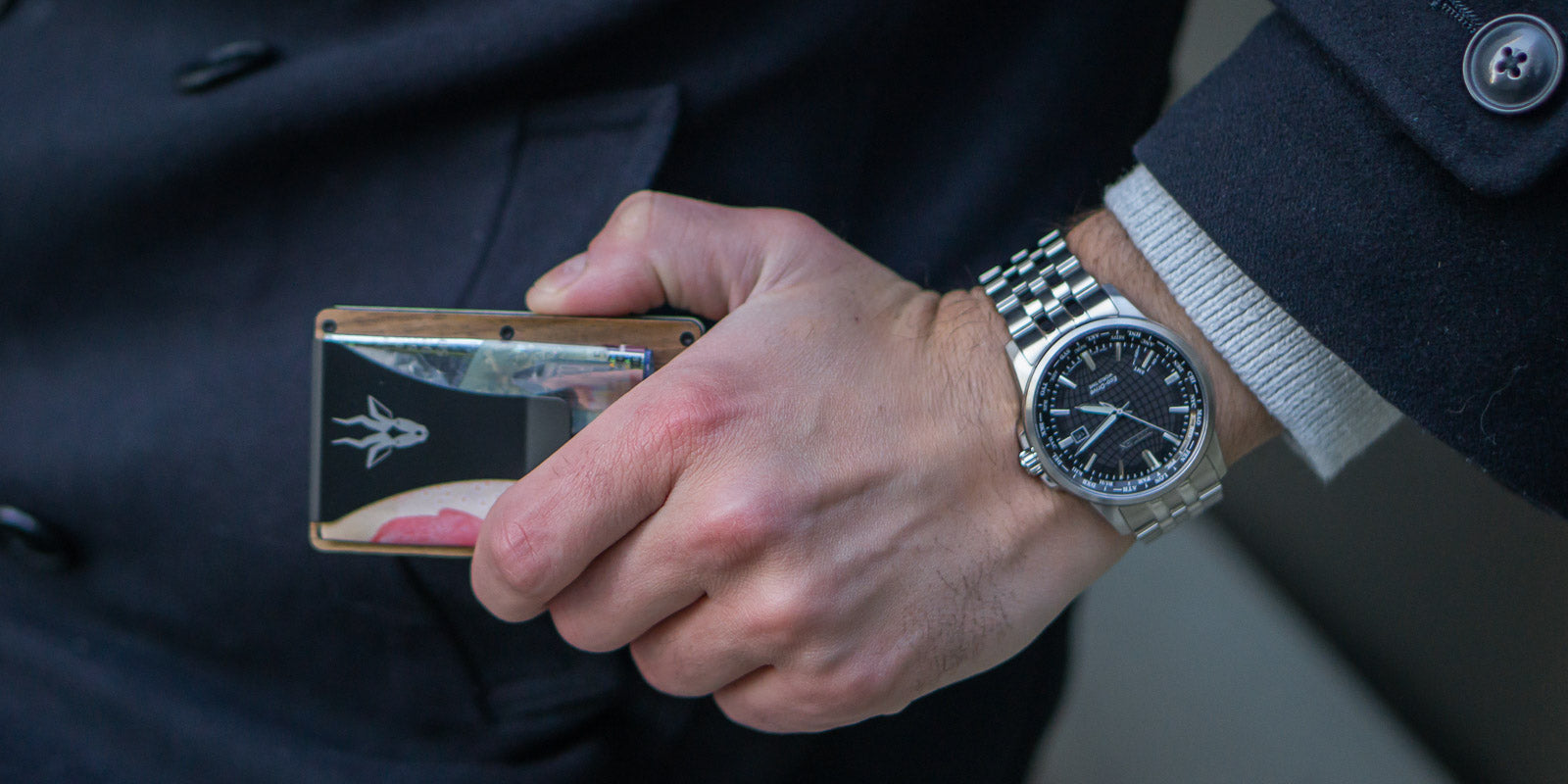 Man Holding Minimal Wood Wallet With Money On Clip Outside Coat Pocket with Silver Watch On Wrist